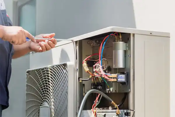 A technician, adept in furnace repair, uses tools to skillfully repair or install an outdoor air conditioning unit with exposed wires.
