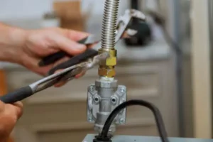 Hands using wrenches to securely tighten a metal hose onto a valve in a mechanical setup, ensuring precision during the gas line installation process.
