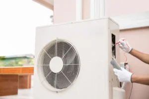 A technician wearing gloves uses a multimeter to test an outdoor heat pump unit, ensuring efficient heat pump maintenance.