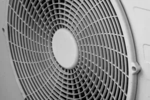 Close-up of a circular ventilation fan with a protective grille, often found in heat pump systems, featuring concentric rings and a central hub.