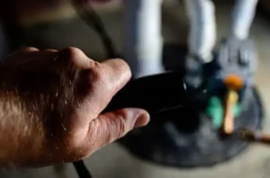 A close-up of a hand holding a black object, likely a TV remote, points toward a blurred screen in the background, reminiscent of the precision needed during sump pump installation.