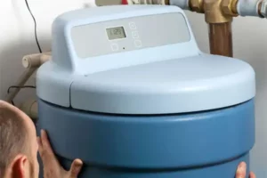 A person expertly adjusts a large blue water softener with a digital control panel on top, ensuring optimal performance.