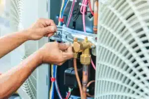 Two hands expertly maneuver tools amidst the colored wires and metal parts of an HVAC unit, showcasing skilled air conditioning maintenance.