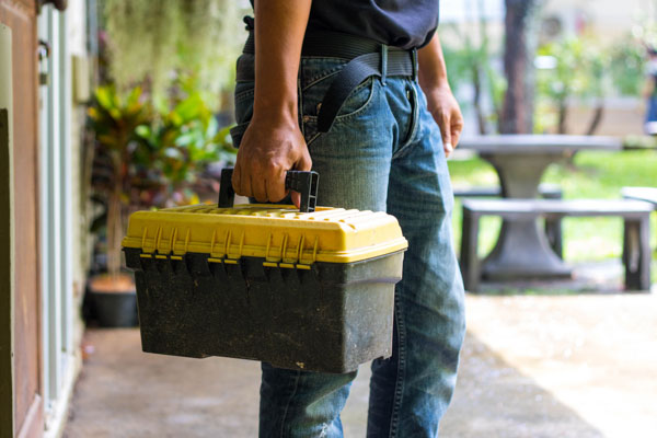 A person in jeans carries a closed black and yellow toolbox, looking ready for an excavation service outdoors. Heating and Cooling Services Colorado: What We Offer Furnace Tune-Up