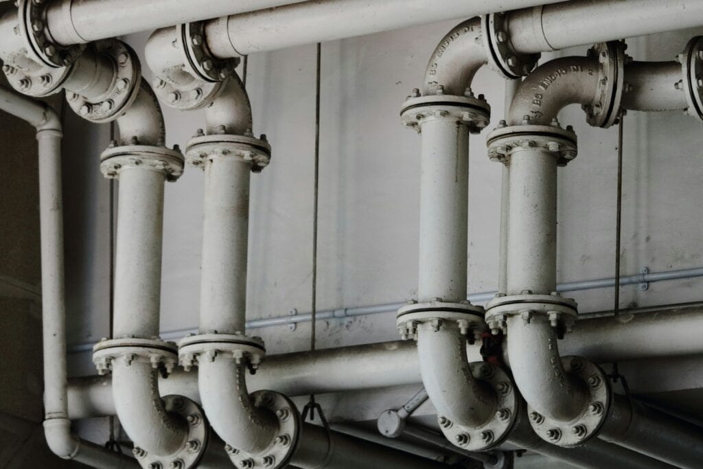A close-up view of several interconnected metal pipes and joints running horizontally and vertically along a wall.